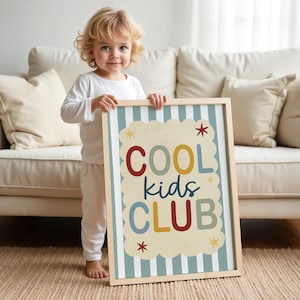 May include: A framed sign with the words "COOL kids CLUB" in colorful letters. The sign has a light wood frame and a striped background with a cloud-shaped border. The sign is held by a young child.