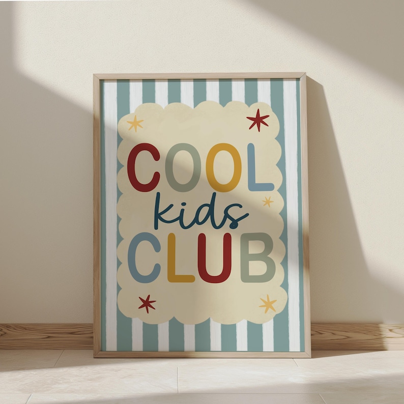 May include: A framed art print with the words "COOL kids CLUB" in colorful letters. The text is on a cream-colored cloud-shaped background with star accents, set against a striped blue and white background. The frame is a light wood color.