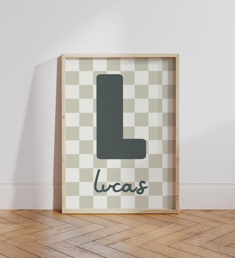 Puede incluir: Un estampado enmarcado con una gran letra "L" gris oscuro sobre un fondo a cuadros de cuadrados grises claros y crema. El nombre "Lucas" est&aacute; escrito en cursiva debajo. El marco es de color madera clara.