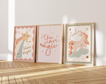 May include: Three framed art prints with a whimsical theme. One features a star with the text "Shine bright", another says "You are magic", and the third has a unicorn and the name "Amelia". The prints have a soft color palette of pink, gold, and blue.