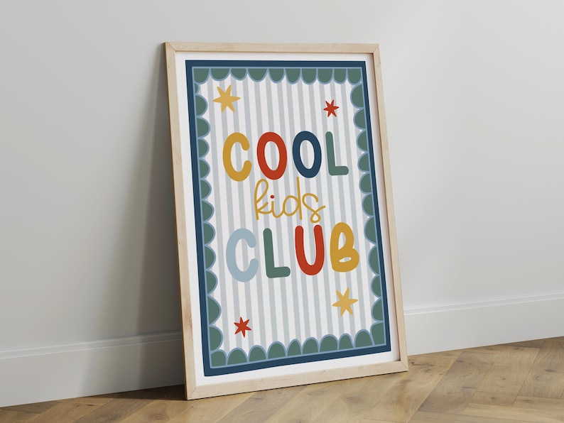 May include: A framed print with the words "COOL kids CLUB" in colorful, playful lettering. The background has vertical stripes, and the frame is light wood. Decorative stars and a scalloped border complete the design.