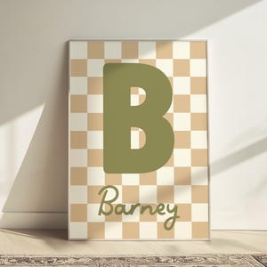 Puede incluir: Arte mural enmarcado con una gran letra "B" verde oliva sobre un fondo a cuadros beige y crema. El nombre "Barney" est&aacute; escrito en cursiva debajo de la letra.