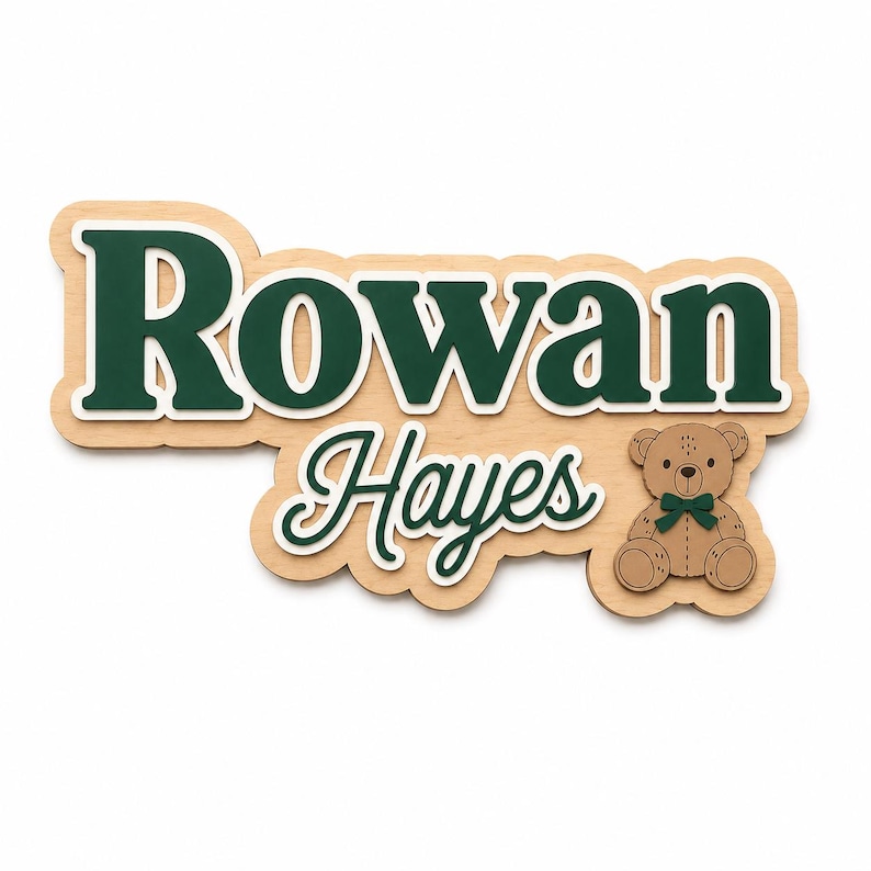 Puede incluir: Letrero de nombre de madera con el nombre "Rowan Hayes" en verde con un contorno blanco. Un peque&ntilde;o oso de peluche con pajarita verde est&aacute; a la derecha. El letrero es de madera clara.