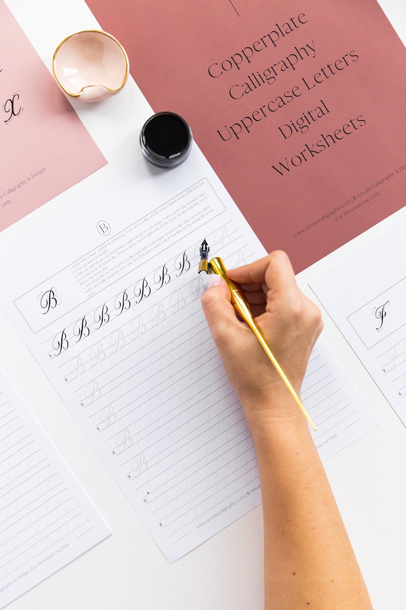 May include: Copperplate calligraphy uppercase letter B practice worksheet with a hand holding a calligraphy pen and ink. The worksheet has a light gray background with a grid pattern and the letter B is written in black ink.