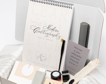 Può includere: Un kit di calligrafia in una scatola con un blocco di pratica, pennini, inchiostro e un biglietto di benvenuto che dice "Benvenuto nella tua avventura di calligrafia. Goditi il processo."