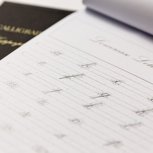 May include: A close-up of a page from a calligraphy practice book. The page is divided into lines with the heading "Lowercase Letters". The letters "a", "b", "c", "d", "e", "f", "g", "h", "i", "j", "k", "l", "m", "n", "o", "p", "q", "r", "s", "t", "u", "v", "w", "x", "y", and "z" are written in cursive on the page.