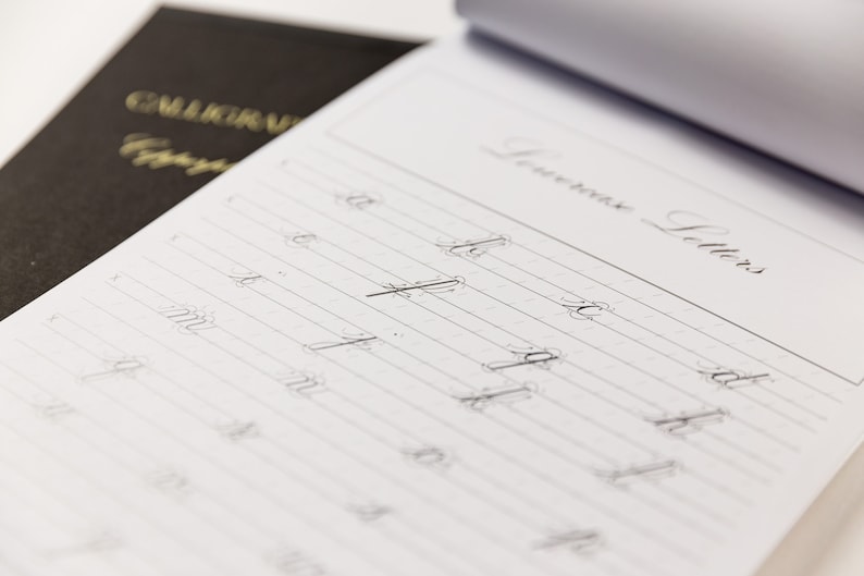 May include: A close-up of a page from a calligraphy practice book. The page is divided into lines with the heading "Lowercase Letters". The letters "a", "b", "c", "d", "e", "f", "g", "h", "i", "j", "k", "l", "m", "n", "o", "p", "q", "r", "s", "t", "u", "v", "w", "x", "y", and "z" are written in cursive on the page.