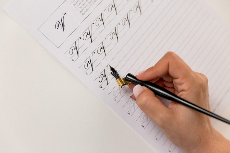 May include: A person practicing calligraphy with a black and gold calligraphy pen on a lined paper. The paper has the letter 'W' written at the top and several lines of the letter 'W' written below.