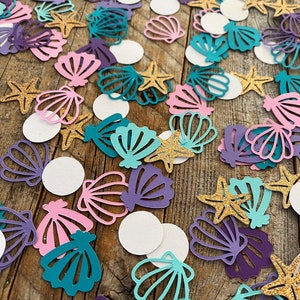 May include: Assortment of colorful paper confetti featuring seashells, starfish, and circles. The confetti is perfect for adding a whimsical touch to any party or celebration.