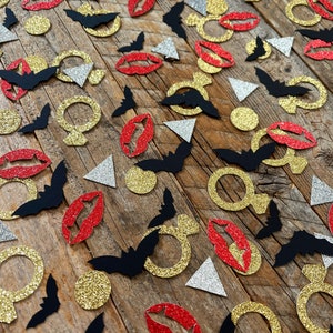 May include: A variety of confetti pieces in black, gold, silver, and red. The confetti includes bats, rings, lips, and triangles.