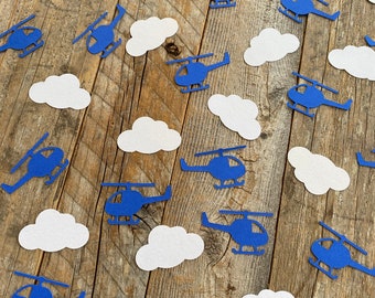 May include: Blue paper helicopter confetti with white paper cloud confetti on a wood background.