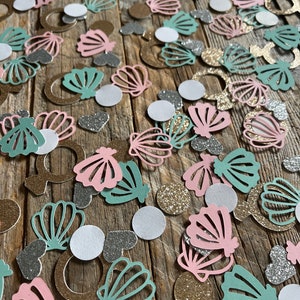 May include: A variety of confetti featuring seashells in pink, green, and gold, along with white and silver glitter hearts and circles.
