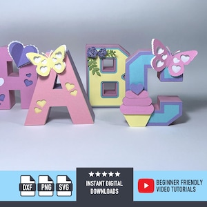May include: Three-dimensional paper letters A, B, and C in pastel colors. The letter A is pink with a yellow butterfly and heart cutouts. The letter B is yellow with purple flowers. The letter C is blue with a pink butterfly and cupcake.