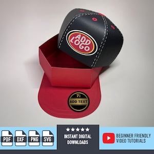 Puede incluir: Una caja con forma de gorra de béisbol negra y roja con el texto "ADD LOGO" en la parte superior y "ADD TEXT" en el borde. La caja es de papel y tiene un diseño cosido en blanco. La caja está abierta.