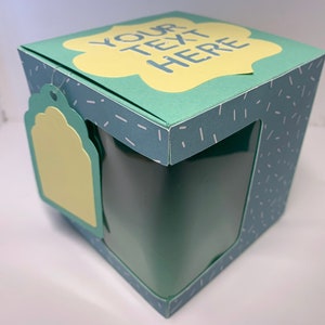 May include: A teal gift box with a clear window and a decorative tag. The box features a light green cloud-shaped label with the text "YOUR TEXT HERE". The box has a pattern of small white dashes.