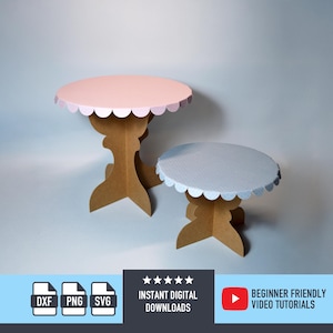 Puede incluir: Dos mesas decorativas de cartón. Una tiene una tapa rosa con borde festoneado, la otra tiene una tapa azul claro con borde festoneado. Ambas tienen bases marrones ornamentadas. La imagen incluye el texto "DESCARGAS DIGITALES INSTANTÁNEAS" y "TUTORIALES EN VÍDEO PARA PRINCIPIANTES."