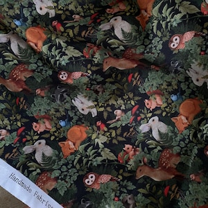 May include: Black fabric with a repeating pattern of white rabbits, brown deer, owls, squirrels, mushrooms, and red birds in a forest setting. The fabric has the text "Handmade Fabrics, Inc. &copy; All Ri" printed on the bottom edge.