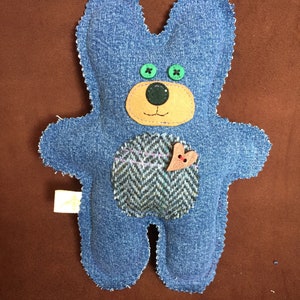 May include: A blue denim teddy bear with green button eyes, a brown felt nose, and a brown felt heart on its chest. The bear is made from recycled denim and has a patchwork design.