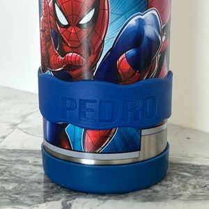 K&ouml;nnte beinhalten: Eine blaue Wasserflasche mit einem Spiderman-Design und einem blauen Band um die Mitte, auf dem "PEDRO" steht.