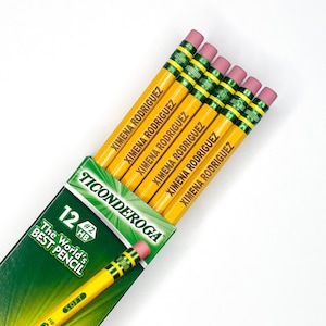 May include: A pack of 12 yellow pencils with green and black accents. The pencils are sharpened and have pink erasers. The pencils are labelled "Ticonderoga" and "The World's Best Pencil". Each pencil is personalised with the name "Ximena Rodriguez".