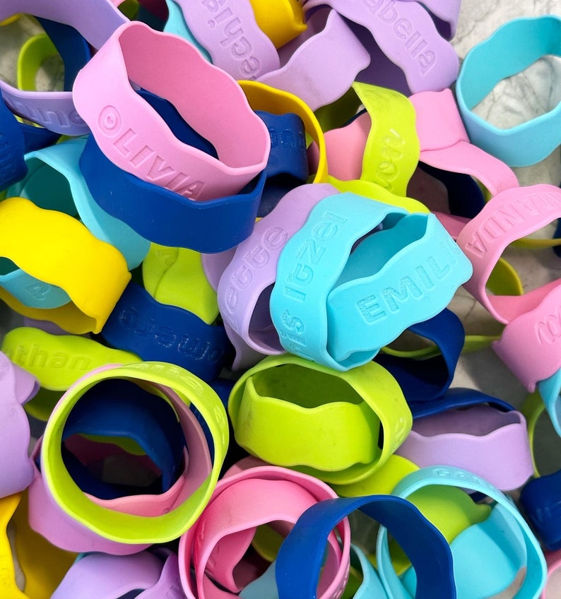 K&ouml;nnte beinhalten: Eine Sammlung bunter Silikon-Armb&auml;nder mit verschiedenen Namen, darunter "Olivia", "Emilie", "Is Izea", "Rebecca", "Amelia" und "Tilda".