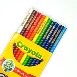 May include: A box of Crayola crayons with the name "XIMENA RODRIGUEZ" written on each crayon. The box is yellow with the Crayola logo and the text "Made with Reforested Wood".