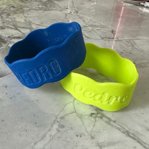 K&ouml;nnte beinhalten: Zwei Silikon-Armb&auml;nder mit dem Namen "Pedro" in Pr&auml;gung. Die Armb&auml;nder sind blau und gr&uuml;n.