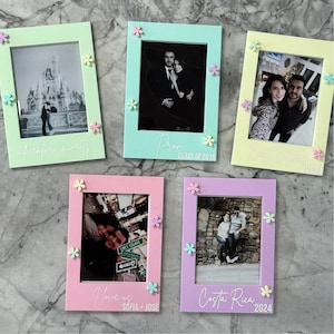 May include: Five colorful picture frames with photos and floral embellishments. The frames are pastel green, blue, yellow, pink, and purple. Each frame has a photo and text, including "adventure awaits!", "Prom CLASS OF 2018", "I love us SOFIA + JOSE", and "Costa Rica 2024".