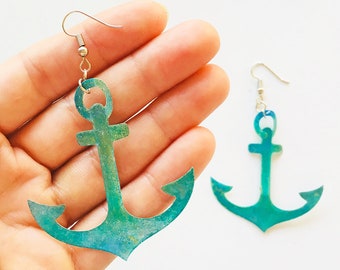 May include: A pair of turquoise blue anchor earrings with silver hooks. The anchors are made of metal and have a textured finish.