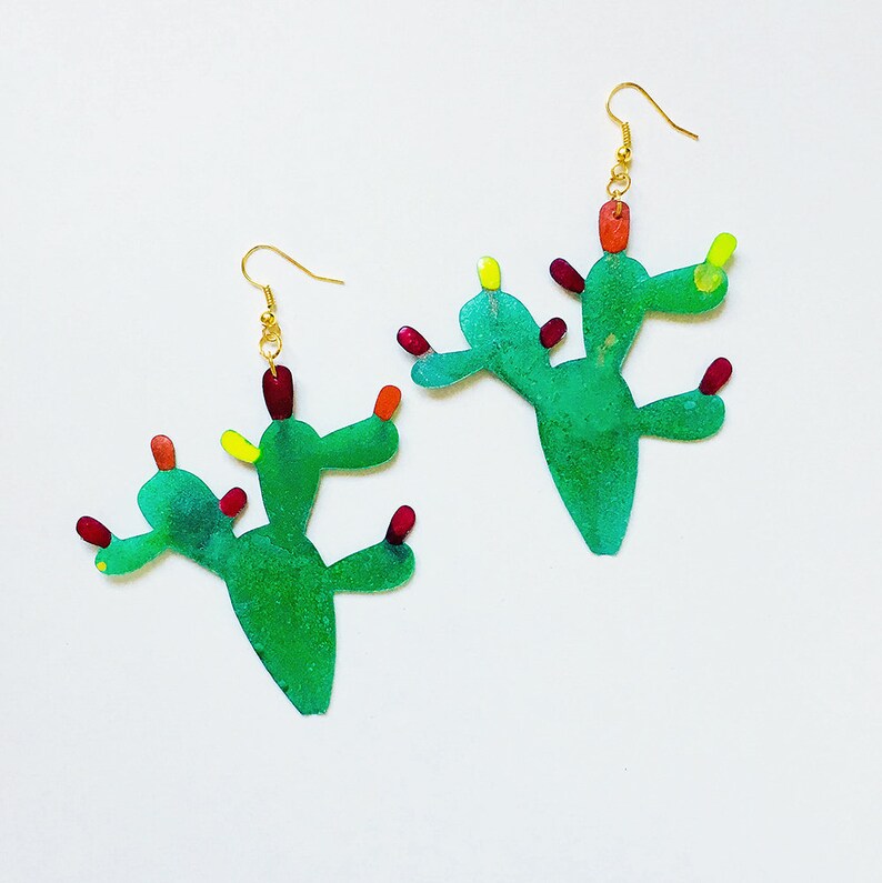 May include: A pair of green cactus earrings with red and yellow accents. The earrings are made of resin and have a gold hook.