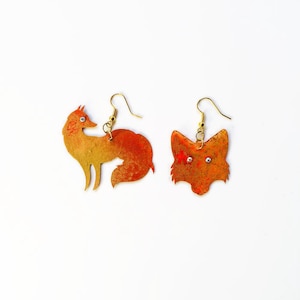 May include: A pair of fox-shaped earrings with gold-toned metal and orange and yellow paint. The earrings have small clear rhinestones for eyes.