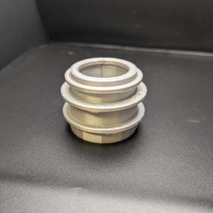 Puede incluir: Tres anillos plateados apilados, cada uno con un di&aacute;metro ligeramente diferente, creando una forma cil&iacute;ndrica.