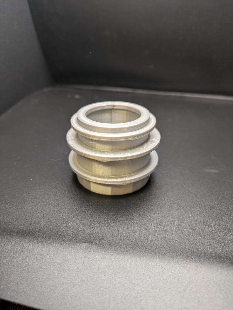 Puede incluir: Tres anillos plateados apilados, cada uno con un di&aacute;metro ligeramente diferente, creando una forma cil&iacute;ndrica.