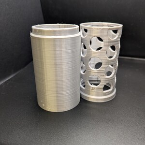 Puede incluir: Dos contenedores cil&iacute;ndricos impresos en 3D. Uno es s&oacute;lido y el otro tiene un patr&oacute;n de agujeros.