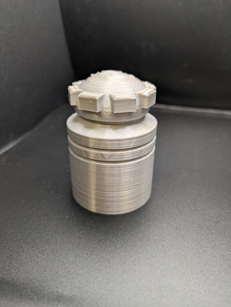 Puede incluir: Un tap&oacute;n de botella de color plateado, impreso en 3D, con un dise&ntilde;o texturizado y estriado. El tap&oacute;n tiene una parte superior circular con un patr&oacute;n de engranaje.
