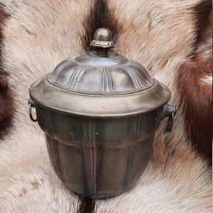 Può includere: Un secchiello per il ghiaccio in ottone vintage con un coperchio e due manici. Il secchiello ha un design scanalato e una manopola decorativa sul coperchio.