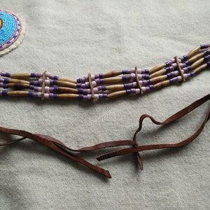 May include: A brown leather choker necklace with five rows of beads. The beads are a mix of light brown wooden beads and small purple and white glass beads.