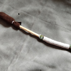 Könnte beinhalten: Ein mit braunem Leder umwickelter Stock mit weißen und grünen Perlen. Der Stock ist etwa 30 cm lang.