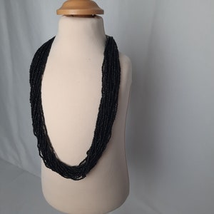Può includere: Una collana di perline nere su un manichino bianco. La collana è composta da molti fili di piccole perline nere.