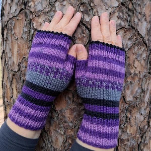May include: A pair of knitted fingerless gloves in shades of purple, gray, and black. The gloves have a striped pattern and a black ribbed cuff. The gloves are designed to keep hands warm while leaving fingers free.