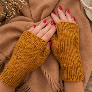 May include: A pair of mustard yellow fingerless gloves featuring a vertical cable knit pattern and ribbed cuffs. The gloves are constructed with a textured knit stitch and have an opening for the thumb, providing coverage for the palm and wrist area.