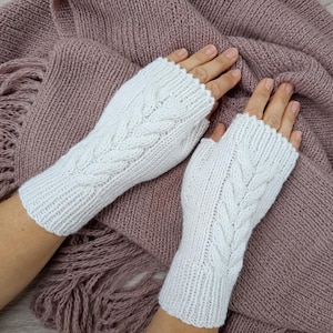 May include: A pair of white fingerless gloves featuring a vertical cable knit pattern on the back of the hand and a ribbed cuff at the wrist. The gloves are crafted from a soft yarn and provide coverage for the palm while leaving fingers exposed.