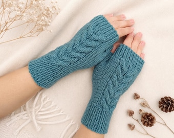 May include: A pair of teal fingerless gloves featuring a vertical cable knit pattern running down the center. The gloves are constructed with a ribbed cuff at the wrist and an open design at the fingers, showcasing a textured knit fabric.