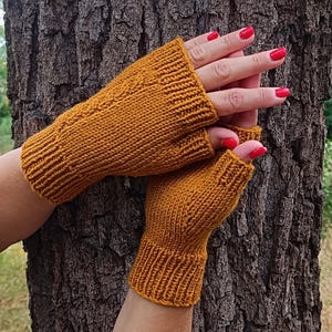 May include: Mustard yellow fingerless gloves, knitted with a textured pattern. The gloves are made of a soft, warm material, perfect for cool weather. The gloves are shown against a tree trunk.