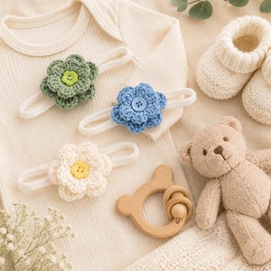 May include: A cream-colored ribbed bodysuit, three elastic headbands with crocheted flowers in green, blue, and cream with matching buttons, a pair of cream knit booties, a wooden bear-shaped teether, and a small plush teddy bear.