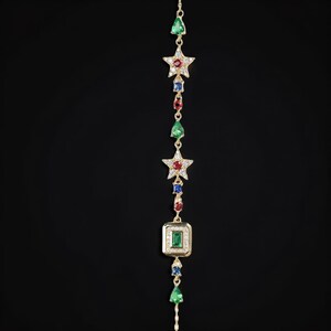 May include: A gold chain bracelet with a star and square pendant set with green, red, and blue gemstones.