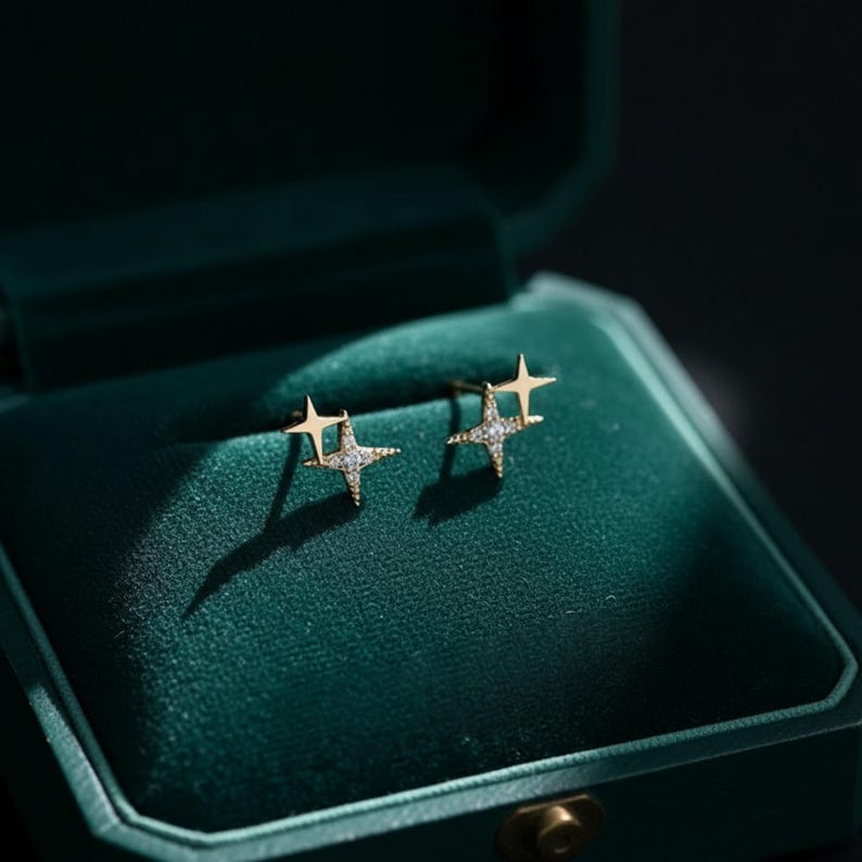 May include: A pair of gold star-shaped stud earrings, each set with small, sparkling gemstones. The earrings are presented in a dark green velvet jewellery box. The earrings are a delicate and elegant accessory, perfect for adding a touch of sparkle.