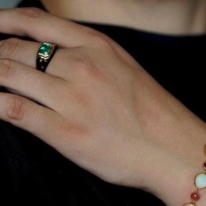 May include: A gold ring with a green gemstone set in a black enamel band. A gold bracelet with oval-shaped white opals and red gemstones.
