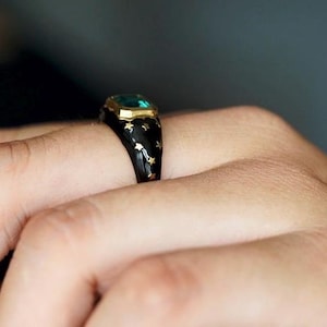 May include: A black ring with gold stars and a green gemstone set in a gold bezel.