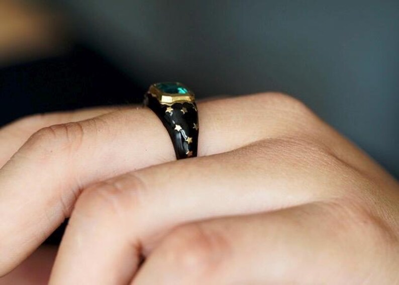 May include: A black ring with gold stars and a green gemstone set in a gold bezel.